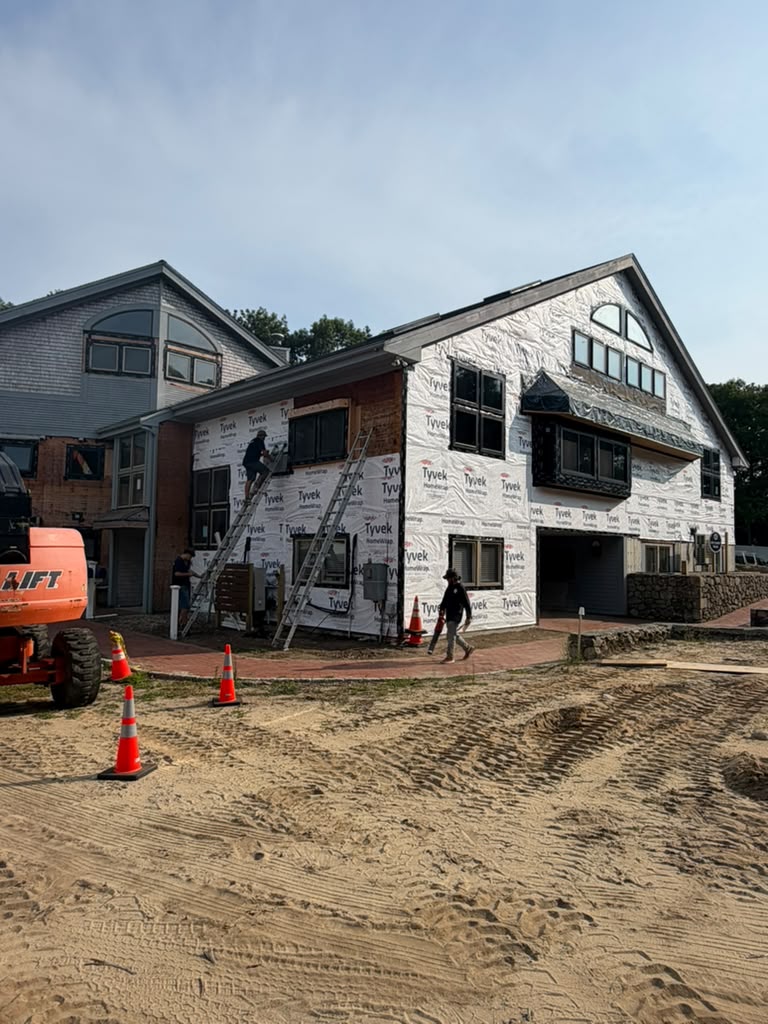 Crew on ladders installing house wrap across a large two story home exterior