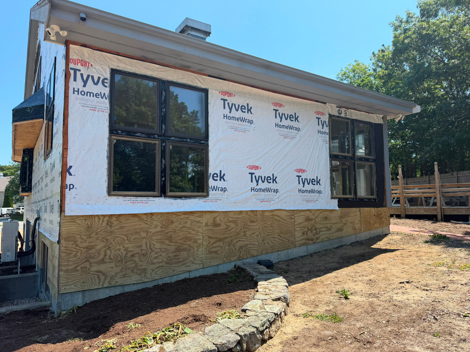 Modern home exterior with house wrap, plywood skirt and new black framed windows