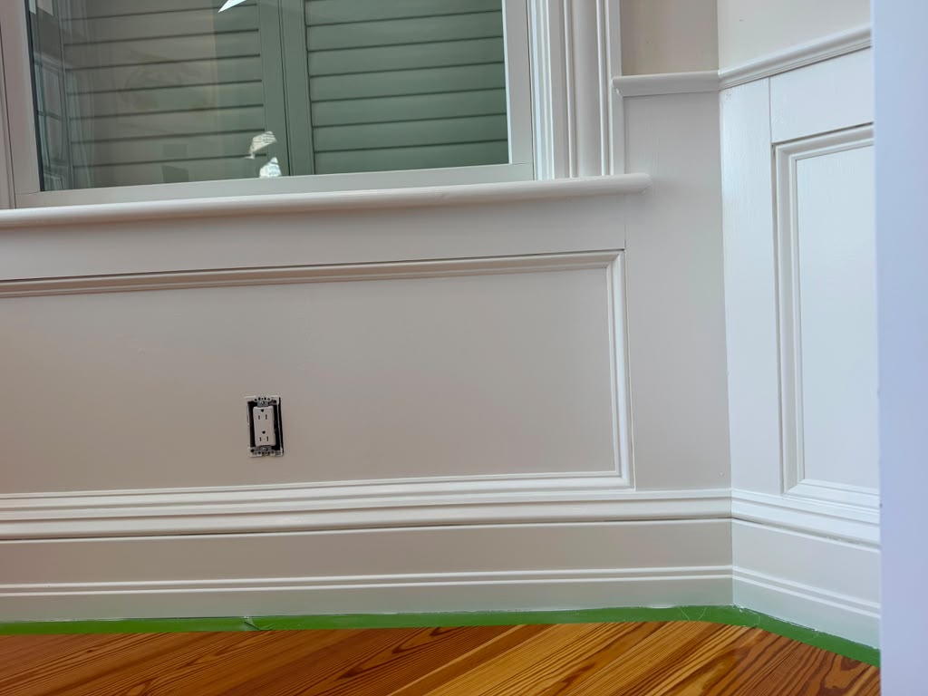 Freshly painted white wainscoting and baseboard trim along hardwood flooring