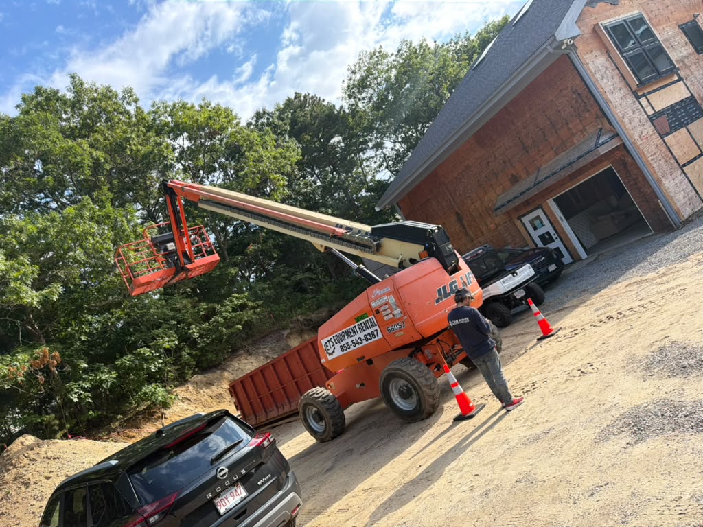 Boom lift and jobsite dumpster staged beside a home under exterior renovation