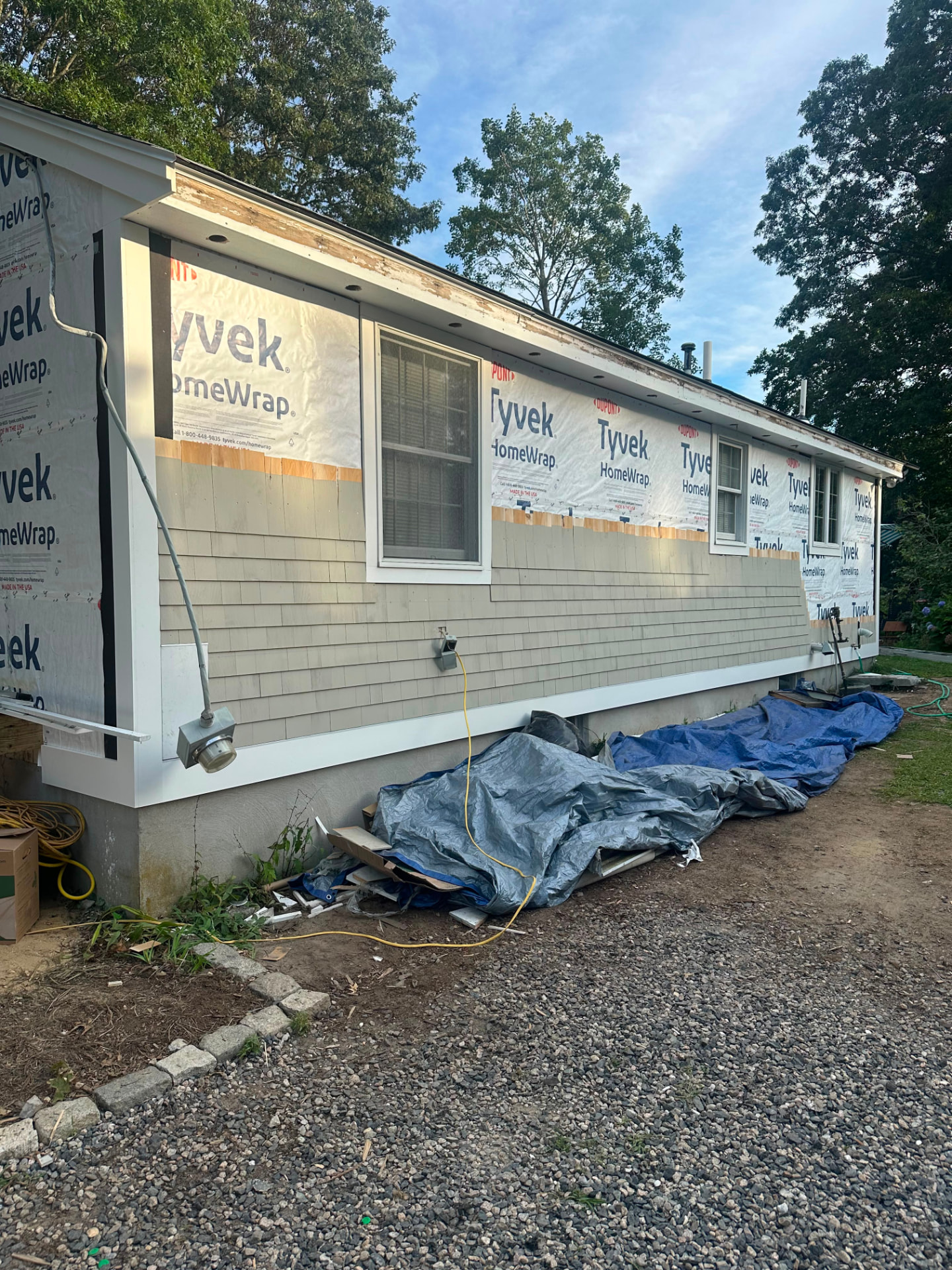 Ranch home with old shingle siding partially removed and new house wrap installed