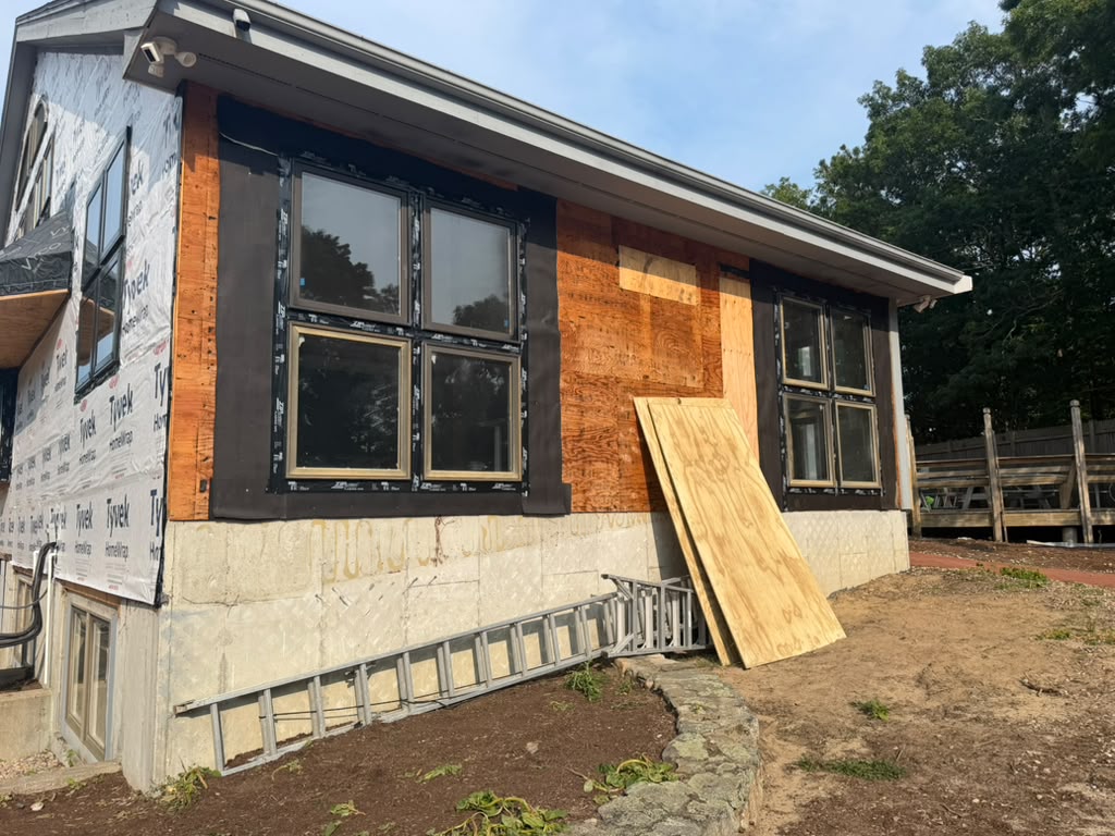 Home exterior with new black framed windows, plywood sheathing and house wrap during siding work
